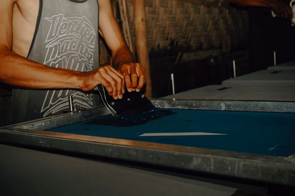 A printer drawing a squeegee loaded with dark blue ink across a screen on a print table.